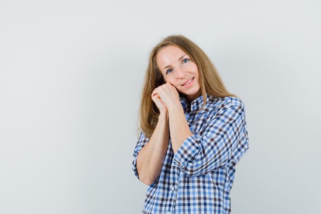 Blonde lady leaning cheek on clasped hands in shirt and looking cute ,