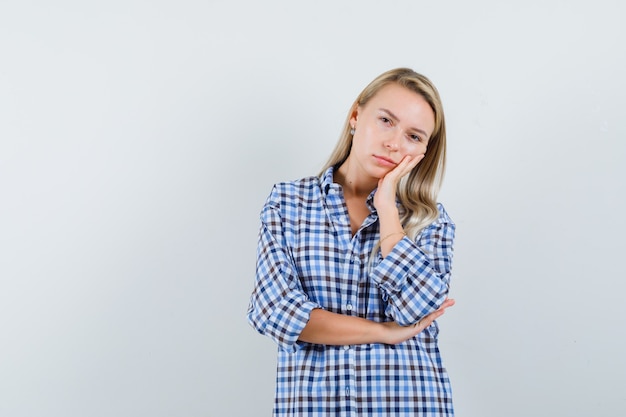 Blonde lady leaning cheek on palm in checked shirt and looking tired