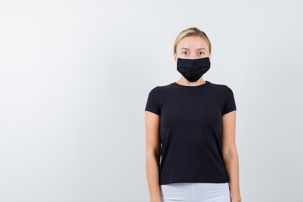 Free photo blonde lady looking at camera in black t-shirt, black mask and looking focused isolated