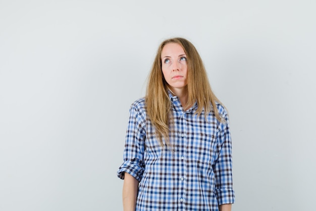 Blonde lady looking up in shirt and looking pensive.