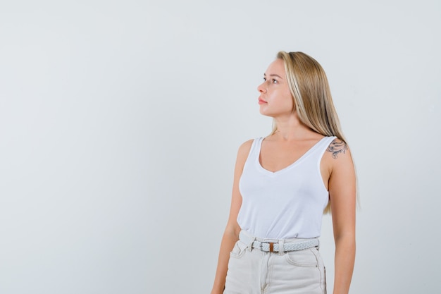 Free photo blonde lady looking up in singlet, pants and looking pensive. front view.