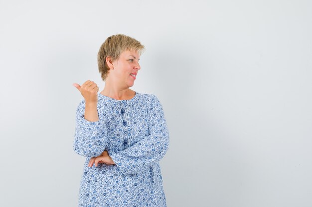 Blonde lady in patterned blouse pointing back , front view. space for text