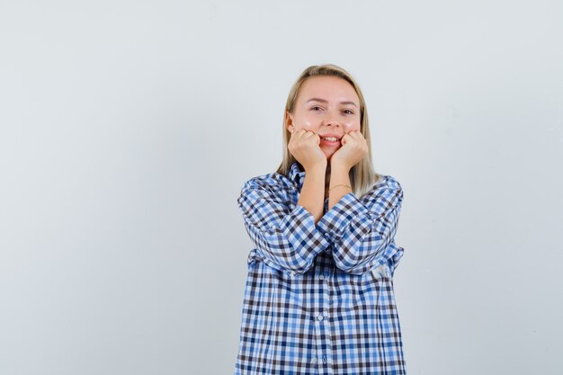 Blonde lady pillowing face on her hands in checked shirt and looking glad