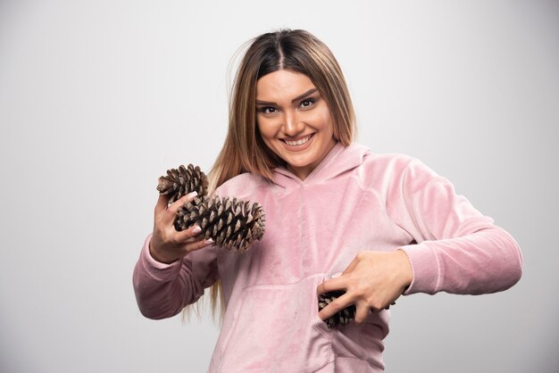 ピンクのスウェットシャツを着た金髪の女性は、樫の木の円錐形を持ってポジティブで幸せな顔をします。