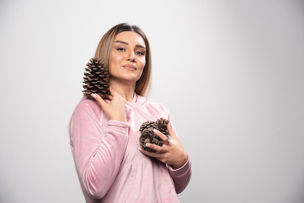 Blonde lady in pink sweatshirt makes positive and happy face by holding oak tree cones.