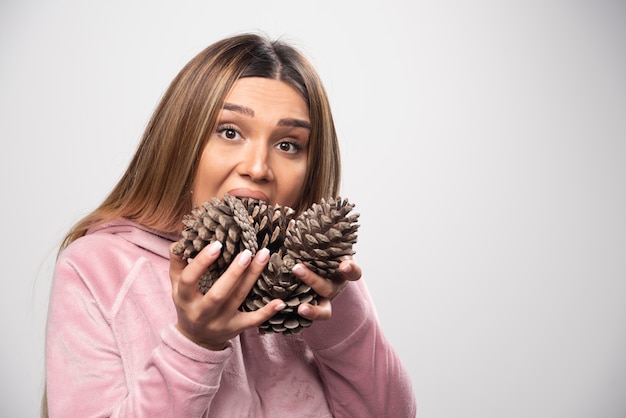 Free photo blonde lady in pink sweatshirt makes silly positive faces with oak tree cones in the hand.