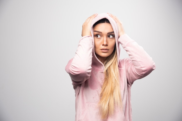 Blonde lady in pink sweatshirt makes terrified and scared face in hoodie.