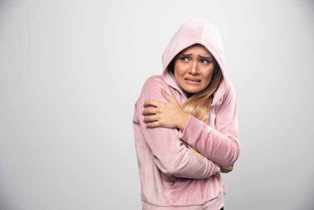 Blonde lady in pink sweatshirt makes terrified and scared face in hoodie.