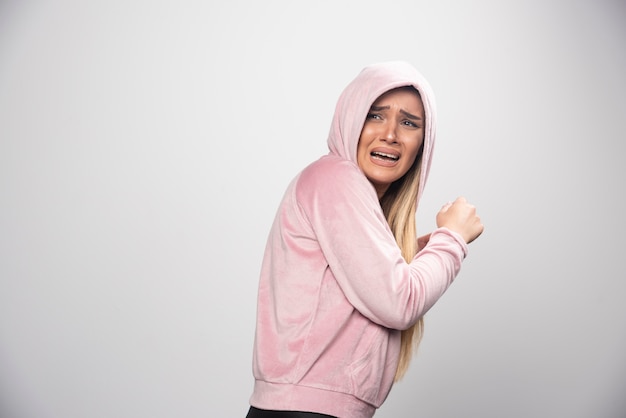 Blonde lady in pink sweatshirt makes terrified and scared face in hoodie.