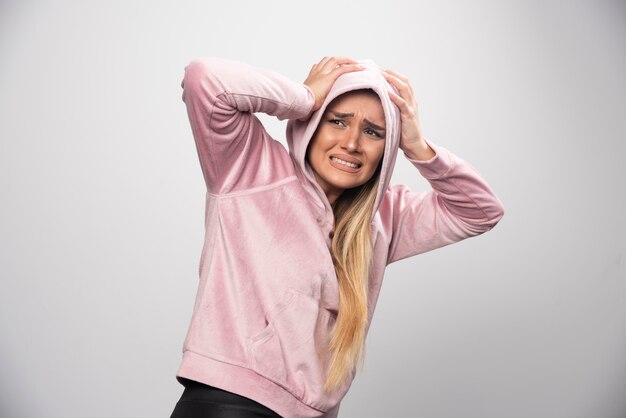 Blonde lady in pink sweatshirt makes terrified and scared face in hoodie.