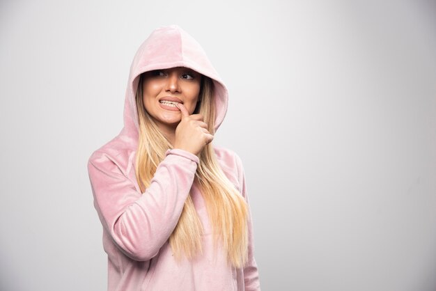 Blonde lady in pink sweatshirt making joyful and positive poses by wearing hoodie to her head.