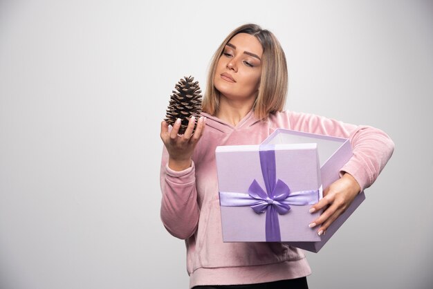 Blonde lady in pink sweatshirt takes out an oak tree cone from the gift box and feels happy.