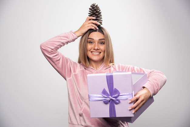 Blonde lady in pink sweatshirt takes out an oak tree cone from the gift box and feels happy.