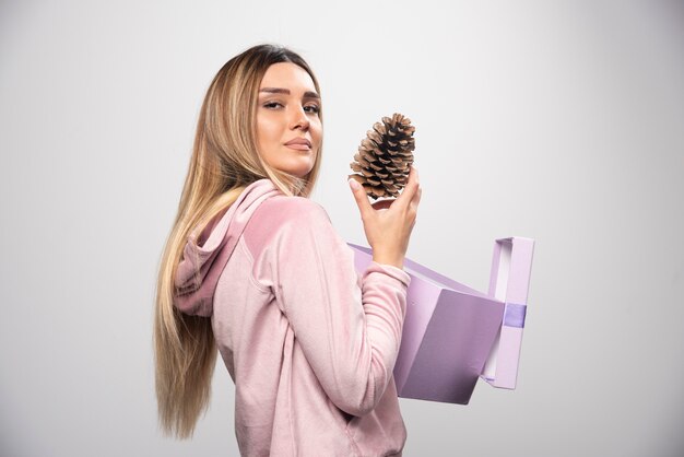 Blonde lady in pink sweatshirt takes out an oak tree cone from the gift box and feels happy.