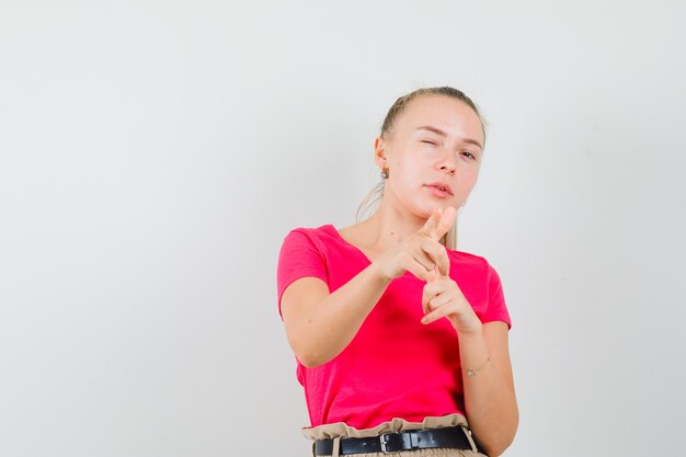 Blonde lady in pink t-shirt pointing at front, winking eye and looking confident , front view.