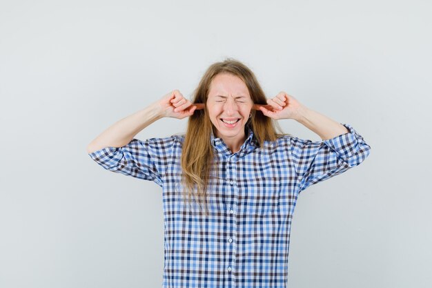 Blonde lady plugging ears with fingers in shirt and looking irritated ,