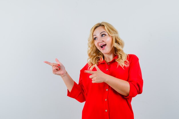 Blonde lady pointing aside in red shirt and looking jolly.