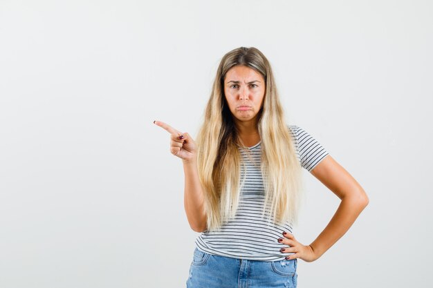 Blonde lady pointing aside in t-shirt and looking upset , front view.