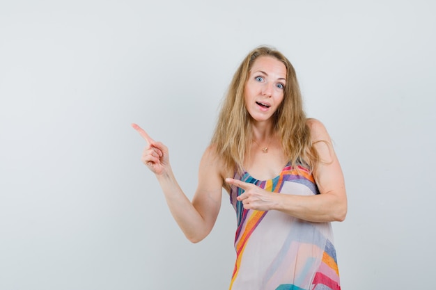 Blonde lady pointing away in summer dress and looking curious 