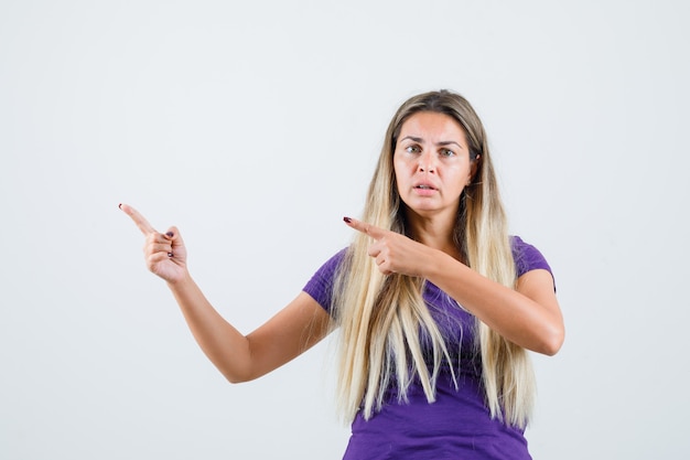 Blonde lady pointing away in violet t-shirt and looking anxious , front view.