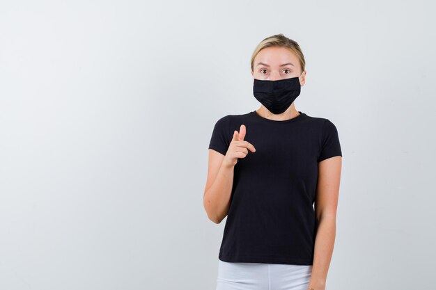 Blonde lady pointing at camera in black t-shirt isolated