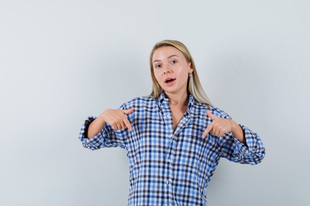 Blonde lady pointing down in checked shirt and looking merry