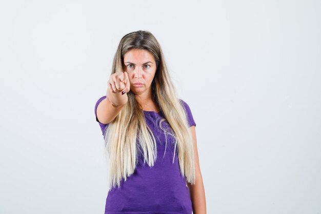 紫のTシャツを着て正面を指して自信を持って見える金髪の女性。正面図。