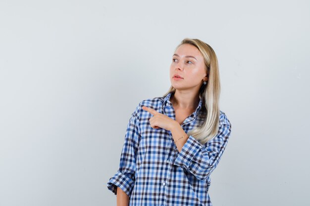 Blonde lady pointing to the left side in checked shirt and looking focused