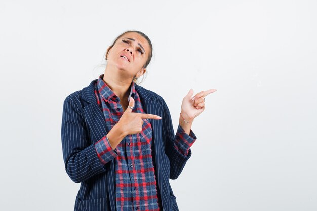 Blonde lady pointing to the right side in shirt, jacket and looking indecisive. front view.