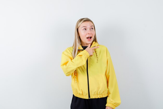 Blonde lady pointing right in tracksuit and looking astonished. front view.