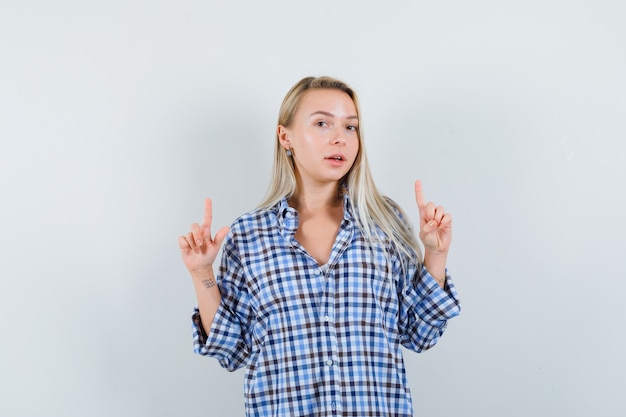 Blonde lady pointing up in checked shirt and looking confident