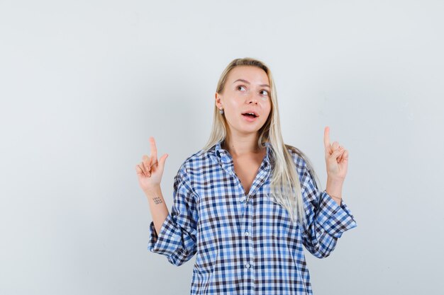 Blonde lady pointing up in checked shirt and looking curious