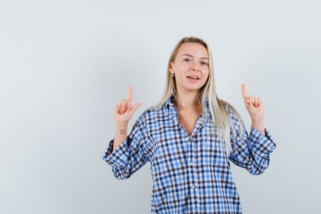 Blonde lady pointing up in checked shirt and looking jolly