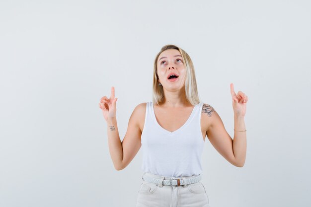 Blonde lady pointing up in singlet, pants and looking hopeful