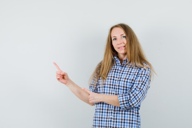 Signora bionda che indica nell'angolo superiore sinistro in camicia e che sembra sicura.