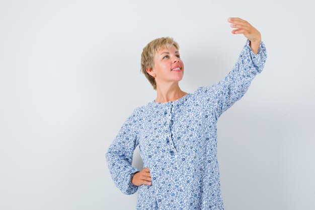 Blonde lady posing like taking selfie photo in patterned blouse and looking happy. front view.