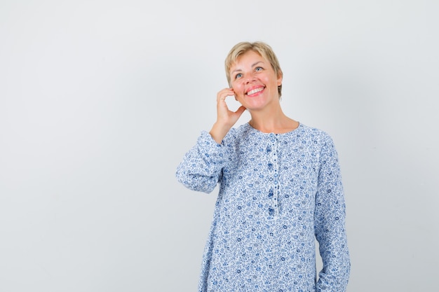 Blonde lady posing like talking on phone in patterned blouse and looking optimistic , front view. space for text