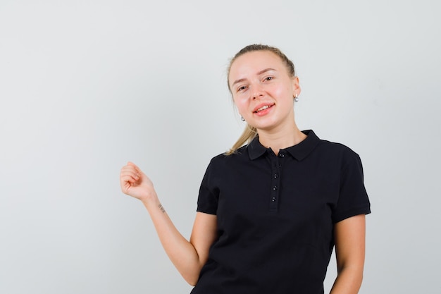 黒のTシャツに立って陽気に見ながらポーズをとる金髪の女性。正面図。