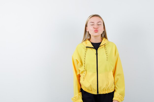 Blonde lady pouting lips, closing eyes in tracksuit and looking cute. front view.