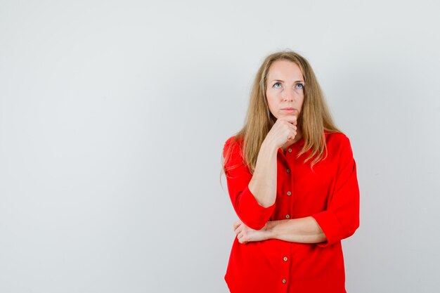 Blonde lady propping chin on fist in red shirt and looking pensive.