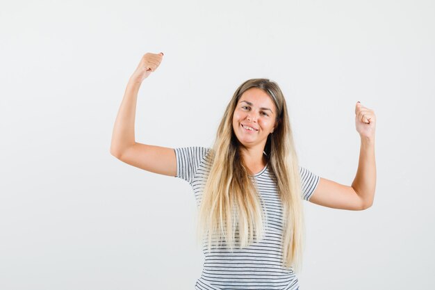 Blonde lady raising her arms in t-shirt and looking energetic , front view.