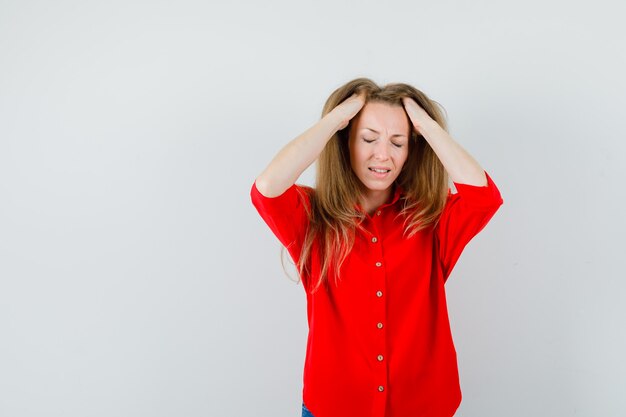 Blonde lady in red shirt holding hands in hair and looking fatigued ,