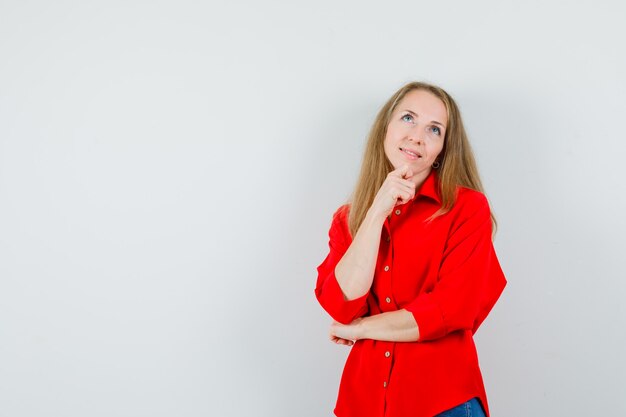 Blonde lady in red shirt propping chin on hand and looking dreamy ,