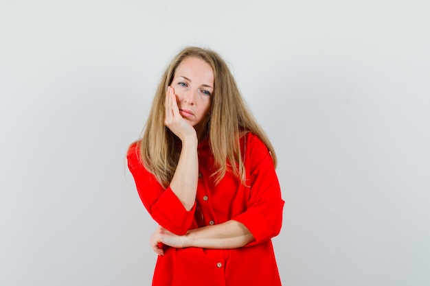 Blonde lady in red shirt propping chin on palm and looking upset ,