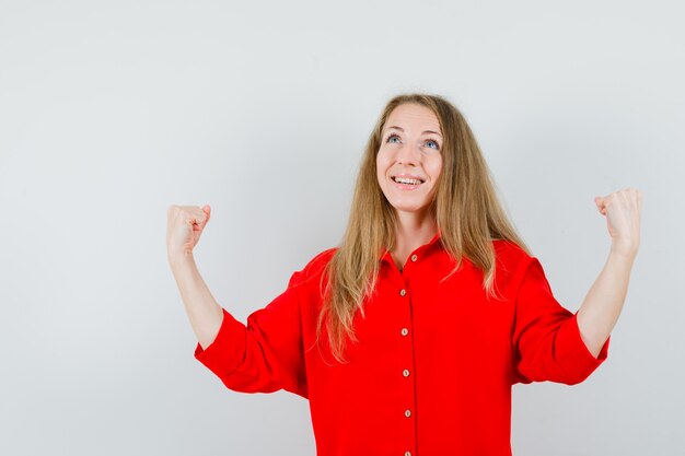 Blonde lady in red shirt showing winner gesture and looking blissful ,