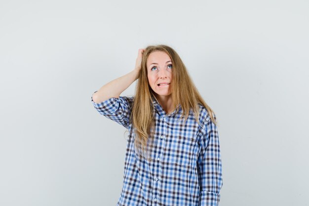 Blonde lady scratching head, biting lip in shirt and looking confused ,