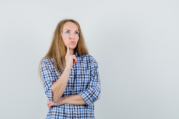 Blonde lady in shirt holding finger on chin and looking pensive ,