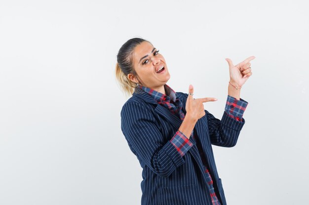 Blonde lady in shirt, jacket pointing at upper right corner and looking cheery , front view.