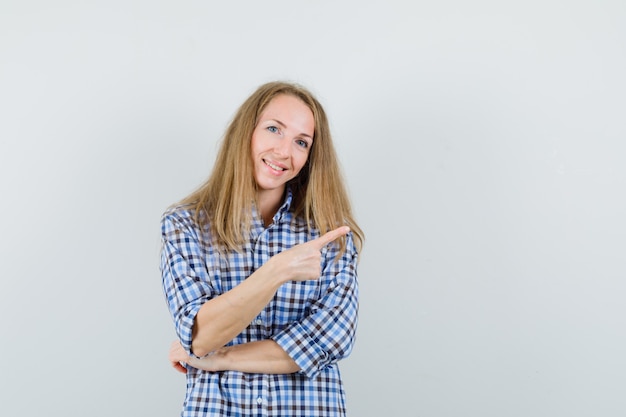 Free photo blonde lady in shirt pointing at upper right corner and looking cheerful ,