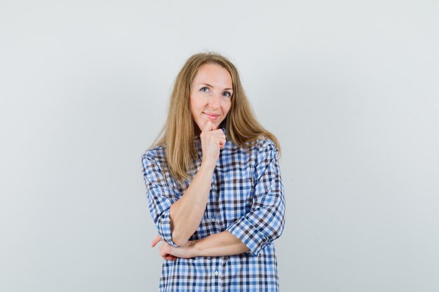 Blonde lady in shirt standing in thinking pose and looking optimistic ,